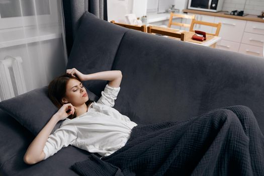 a woman in a white t-shirt lies on the sofa under a blanket and gestures with her hands. High quality photo