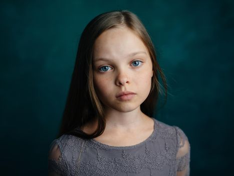 Cute blue-eyed girl in a gray dress on a green background cropped view. High quality photo