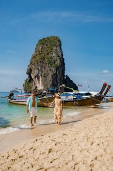 couple mid age on a tropical beach in Thailand, tourist on a white tropical beach, Railay beach with on the background longtail boat. Railay Beach in Krabi province. Ao Nang, Thailand.