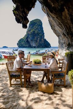 couple mid age on a tropical beach in Thailand, tourist on a white tropical beach, Railay beach with on the background longtail boat. Railay Beach in Krabi province. Ao Nang, Thailand.