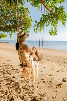 Happy traveler woman in hammock relaxing on the swing and looking beautiful nature, Andaman sea, Krabi, Tourist sea beach Thailand, Asia, Summer holiday vacation travel trip. European man and an Asian woman