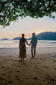 couple watching the sunset on the beach, European man and Asian woman sunset on the beach in Krabi Thailand. Asia