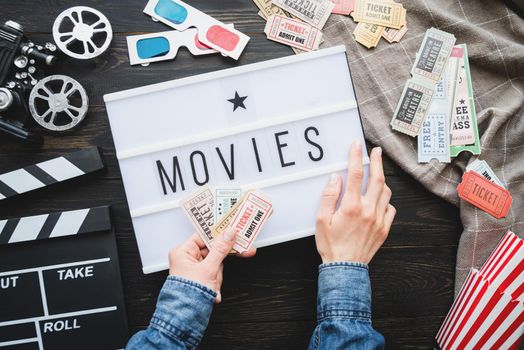 Retro and vintage. Old school film reel projector, lightbox with word Cinema, clapper board. Woman hands holding vintage movie tickets, top view flat lay