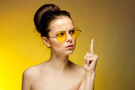 pretty woman in yellow glasses naked shoulders gestures with hands emotions. High quality photo