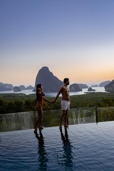 couple men and woman mid age watching sunrise in Phangnga bay Thailand, Phangan bay viewpoint, couple watching sunrise on the edge of a swimming pool, infinity pool look out over Phangnga Bay Thailand