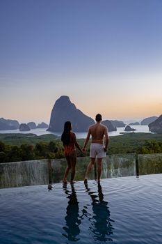 couple men and woman mid age watching sunrise in Phangnga bay Thailand, Phangan bay viewpoint, couple watching sunrise on the edge of a swimming pool, infinity pool look out over Phangnga Bay Thailand