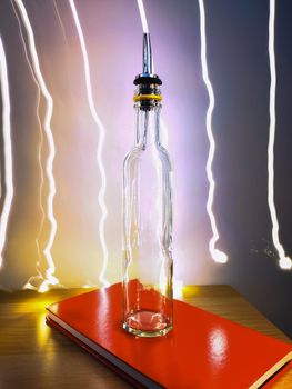 Small narrow bottle with bartender pourer on table with light paiting around
