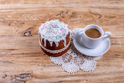Homemade cake, decorated with white icing with decorative sprinkles, lie on a crocheted napkin on a wooden table with a cup of coffee, top and side view.