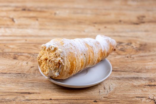 Delicious fragrant puff pastry cone with protein cream or whipped cream on white plate on wooden table