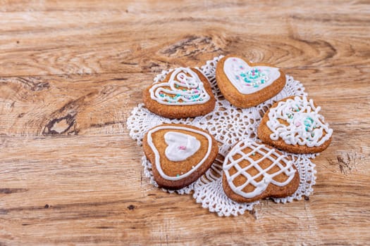 Homemade heart-shaped cookies, decorated with white icing with decorative sprinkles, lie on a crocheted napkin on a wooden table, top view with space for text.