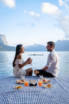 couple having breakfast in front of wooden floating room visiting Khao Sok national park in Phangnga Thailand, Khao Sok National Park, Cheow Lan lake, Ratchaphapha dam. man and woman mid age vacation 