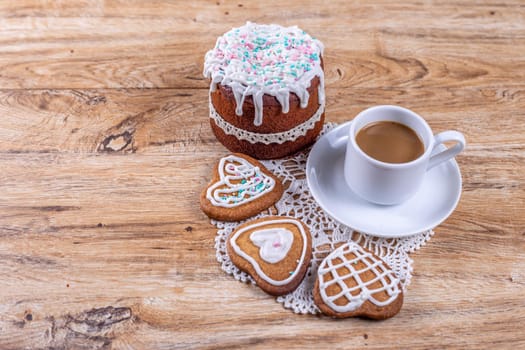 Homemade heart-shaped cookies, decorated with white icing with decorative sprinkles, lie on a crocheted napkin on a wooden table with a cup of coffee, top and side view.