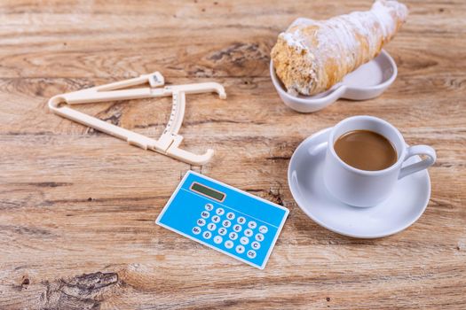 A small coffee cup on a saucer stands on a wooden table next to a notebook and a pen, calculator and caliper, the concept of switching to proper nutrition, losing weight, calculating calories