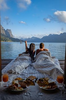 couple having breakfast in front of wooden floating room visiting Khao Sok national park in Phangnga Thailand, Khao Sok National Park, Cheow Lan lake, Ratchaphapha dam. man and woman mid age vacation 