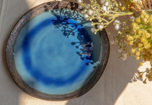 Ceramic plate and flowers on white textured table cloth. Top view, Selective focus.