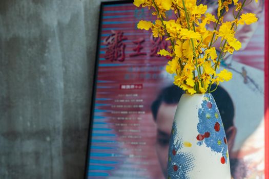 Yellow flowers in Handmade ceramic vase and with Classic chinese poster movie frame with old ruins cement wall. Home decor, Selective focus.