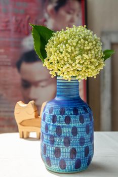 Bangkok, Thailand -Feb 06, 2021 :  Bouquet of flowers in Blue ceramic vase and Wooden doll cat shape on white textured table cloth in front of Classic chinese poster movie frame with old cement wall. Home decor, Selective focus.