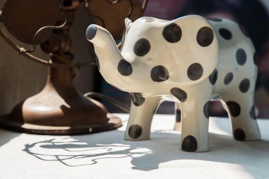 Elephants shaped ceramic and Vintage metal fan on white textured table cloth. Home decor, No focus, specifically.
