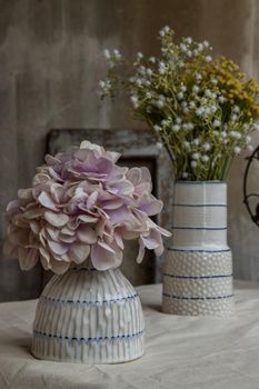 Bouquet of flowers in Two white handmade ceramic vase on white textured table cloth with old cement wall at the balcony house. Home decor, Selective focus.