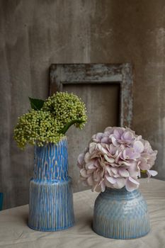 Bouquet of flowers in Two blue handmade ceramic vase on white textured table cloth with old cement wall at the balcony house. Home decor, Selective focus.