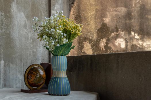 Bouquet of flowers in Blue handmade ceramic vase and globe on white textured table cloth with old cement wall at the balcony house. Home decor, Selective focus.