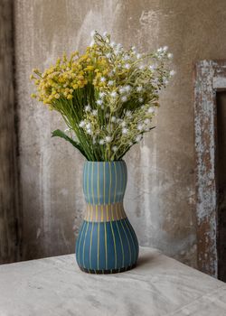 Bouquet of green and white flowers in Blue handmade ceramic vase on white textured table cloth with old cement wall at the balcony house. Home decor, Selective focus.