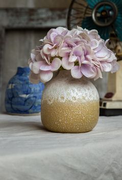 Bouquet of purple flowers in White with yellow handmade ceramic vase and Vintage fan on white textured table cloth with old cement wall. Home decor, Selective focus.