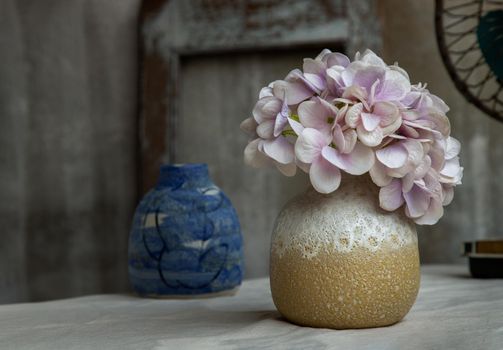 Bouquet of purple flowers in White with yellow handmade ceramic vase and Vintage fan on white textured table cloth with old cement wall. Home decor, Selective focus.