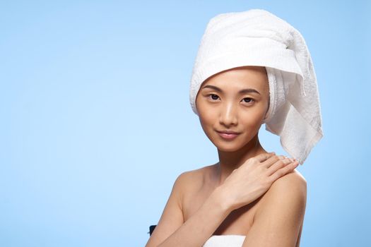 pretty woman asian appearance bare shoulders towel on head spa procedure blue background. High quality photo