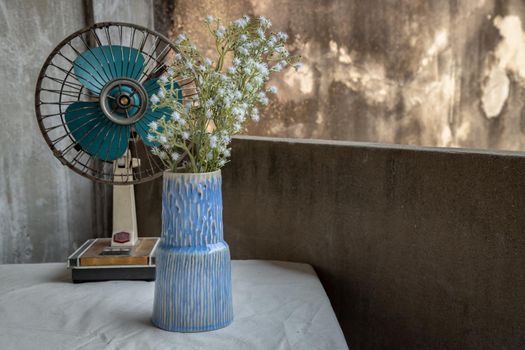 Bouquet of white flowers in Blue handmade ceramic vase and old vintage fan on white textured table cloth with old cement wall at the balcony house. Home decor, Copy space, Selective focus.