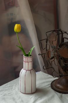 Yellow flower in White handmade ceramic vase and Vintage fan on white textured table cloth with old cement wall. Home decor, Selective focus.