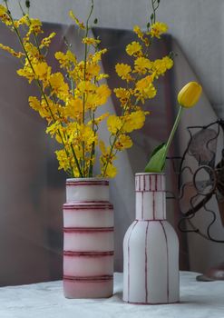 Bouquet of yellow flowers in Two handmade ceramic vase and Vintage fan on white textured table cloth with old cement wall. Home decor, Selective focus.