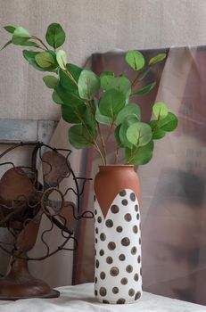 Green leaf in Handmade ceramic vase and Vintage fan on white textured table cloth with old cement wall. Home decor, Selective focus.