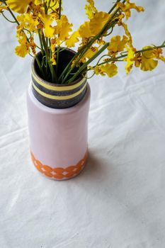 Bouquet of yellow flowers in Handmade ceramic vase and Vintage fan on white textured table cloth. Home decor, Selective focus.