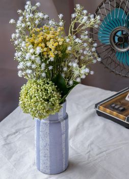 Bouquet of green and white flowers in Handmade ceramic vase and Vintage fan on white textured table cloth. Home decor, Selective focus.