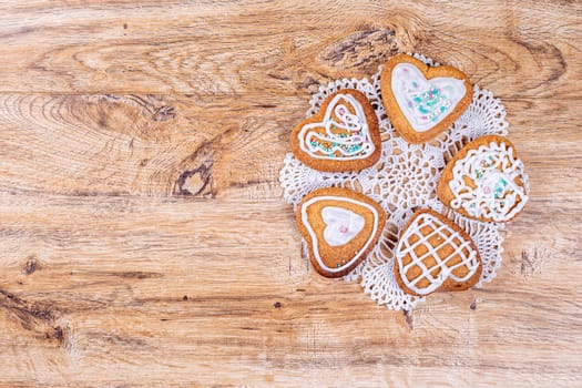 Homemade heart-shaped cookies, decorated with white icing with decorative sprinkles, lie on a crocheted napkin on a wooden table, top view with space for text.