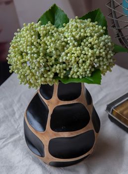Bouquet of green in Handmade wooden vase and Vintage fan on white textured table cloth with old cement wall. Home decor, Selective focus.