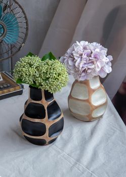 Bouquet of green and purple in Two handmade wooden vase and Vintage fan on white textured table cloth with old cement wall. Home decor, Selective focus.