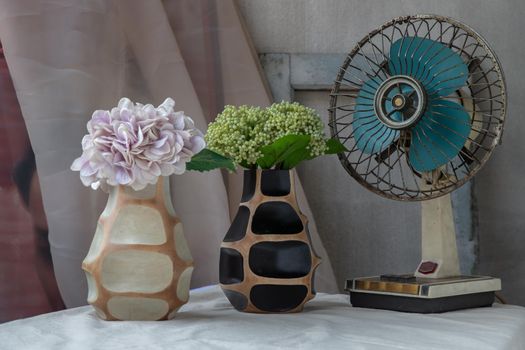 Bouquet of green and purple in Two handmade wooden vase and Vintage fan on white textured table cloth with old cement wall. Home decor, Selective focus.