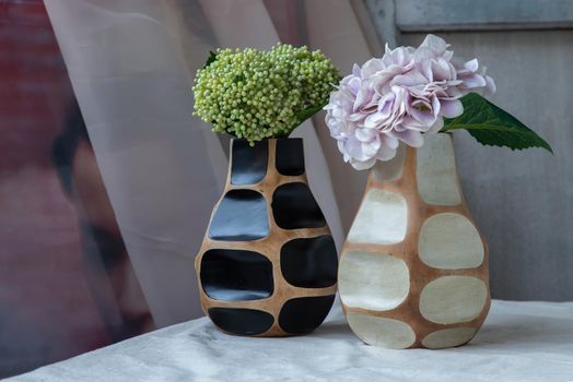 Bouquet of green and purple in Two handmade wooden vase on white textured table cloth with old cement wall. Home decor, Selective focus.