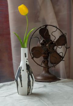 Bangkok, Thailand - Feb 06, 2021 : Yellow flower in Black and White Handmade ceramic vase and Vintage fan on white textured table cloth with old cement wall. Home decor, Selective focus.