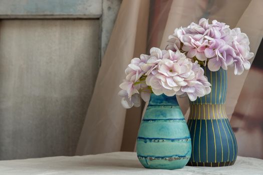Bouquet of purple flowers in Two blue handmade ceramic vase on white textured table cloth. Home decor, Selective focus.