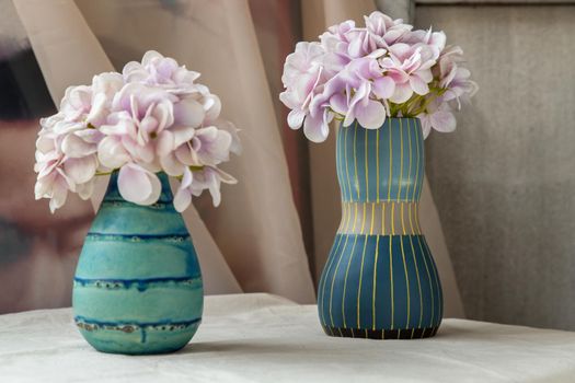 Bangkok, Thailand - Feb 06, 2021 : Bouquet of purple flowers in Two blue handmade ceramic vase on white textured table cloth. Home decor, Selective focus.
