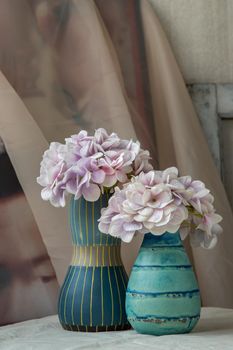 Bangkok, Thailand - Feb 06, 2021 : Bouquet of purple flowers in Two blue handmade ceramic vase on white textured table cloth. Home decor, Selective focus.