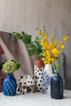Bangkok, Thailand - Feb 06, 2021: Bouquet of many flowers in Handmade Assorted Many Different Ceramic Polka Dotted Vases and Elephant shaped ceramic on white textured table cloth. Home decor, Space for text, Selective focus.