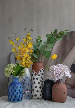 Bouquet of many flowers in Handmade Assorted Many Different Ceramic Polka Dotted Vases on white textured table cloth. Home decor, Space for text, Selective focus.