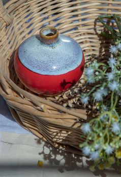 Small red ceramic vases with bouquet of flowers in woven basket. Home decor, Selective focus.