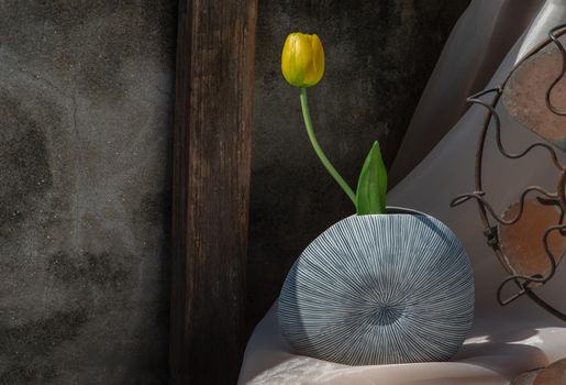Yellow flower in Blue shell shape ceramic vase on pink textured table cloth with old cement wall.