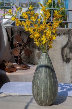 Bouquet of yellow flowers in Green watermel on shape ceramic vase and old vintage fan on pink textured table cloth with old cement wall at the balcony house. Home decor, Selective focus.