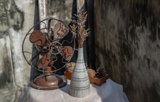 Dried flowers in Ceramic vase on pink textured table cloth and vintage fan with Old cement wall. Home decor, Selective focus.